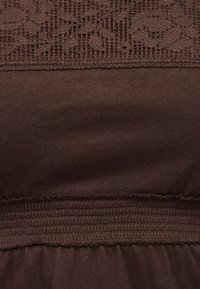 Σκούρο καφέ ύφασμα με δαντελένιο φλοράλ μοτίβο στο πάνω μέρος και λεπτομέρεια με ελαστική ραφή συγκέντρωσης από κάτω.