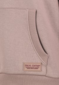 Light pink hoodie featuring a kangaroo pocket, ribbed cuffs, and a textured label with “SBLVL CNTMP” branding. Soft fabric with smooth finish.