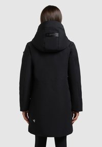 Must kollane isoleeritud parka, millel on kõrge krae ja suur kapuuts. Omab logotähist ja sirget lõiget, ulatudes reie keskele.