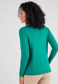 Maglione verde a maniche lunghe con design aderente e texture morbida, caratterizzato da un collo a giro e dettagli di cucitura sottili sulle spalle.