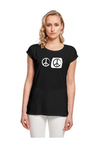Schwarzes Baumwoll-T-Shirt mit kurzen Ärmeln, das zwei Friedenssymbol-Designs in Weiß zeigt, eines umrandet und eines ausgefüllt, zentriert auf der Vorderseite.