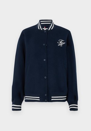 Tumedan navy varsity jakk, millel on valged triibulised ribbed krae, mansetid ja alläär, ees nupud ja valge broderiga "FH" logo rindkeres.