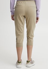Beige capri bukser med elastisk talje og oppbrett, med to baklommer. Materialet ser mykt og strekkbart ut.