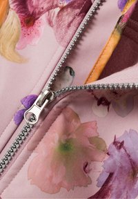 Light pink fabric with floral patterns. Features a silver zipper detail along the edge, exposing an orange inner lining. Soft texture.