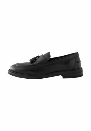 Mocasín de cuero negro con punta redondeada, acento decorativo de metal, detalle de costura en la parte superior y suela plana de goma.