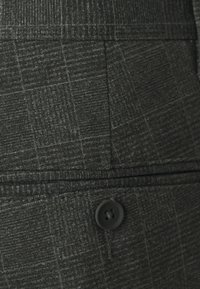Tissu gris foncé avec un motif à carreaux subtil, d'une texture lisse et avec un détail de bouton noir au niveau de la taille.