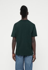 T-shirt en coton vert foncé à manches courtes, col rond et coupe décontractée. Vue de dos montrant une texture lisse et un design simple.