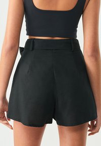 Svarta högmidjade shorts med en slät yta, som har sidofickor och en rosettdetalj i ryggen. Designade för en avslappnad passform.