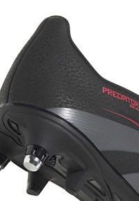 Schwarzer Sportschuh mit strukturiertem Obermaterial, versehen mit rotem Branding. Inklusive profiliertem Sohle mit sichtbaren Stollen und einem grauen Akzentstreifen.