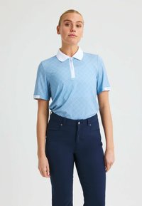 Helles blaues Polohemd mit einem Rautenmuster, weißem Kragen und Logodetails; kombiniert mit dunkelblauen Hosen. Glatte Textur und schmaler Schnitt.