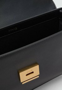 Borsa a mano in pelle nera con una chiusura in tono oro e un logo inciso. L'interno è foderato con un tessuto morbido, che offre un design elegante.