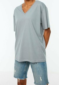 T-shirt grigio a V in cotone morbido con vestibilità rilassata e maniche corte, abbinato a pantaloncini di jeans con bordi sfrangiati e dettagli strappati.