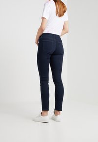 Mörkblå skinny jeans i denim med midja, två bakfickor och en ren, minimalistisk design, kombinerade med vita sneakers.