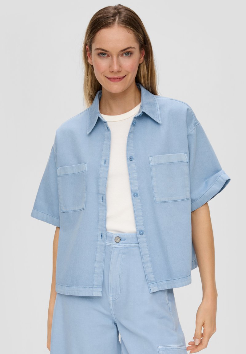 Light blue short-sleeve shirt made of denim, featuring a buttoned front, two chest pockets, and a relaxed fit. Smooth texture.