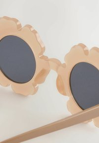 Ochelari de soare în formă de floare au un cadru roz translucid, cu lentile ovale închise la culoare și o textură netedă. Bratele sunt subțiri și de o nuanță neutră.