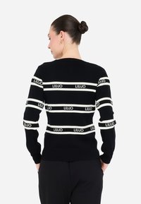Maglione nero in maglia con strisce orizzontali bianche e dettagli di marchio. Silhouette aderente, scollo rotondo e maniche lunghe.