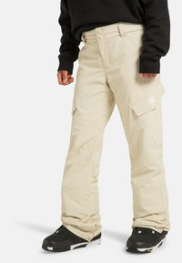 Beige sneeuwbroeken met een ontspannen pasvorm, gemaakt van waterafstotend materiaal, voorzien van cargozakken en een logo-accent op de dij.