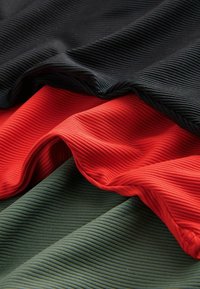 Tissu côtelé noir, rouge et vert foncé, superposé et légèrement froissé, montrant la texture et les plis.