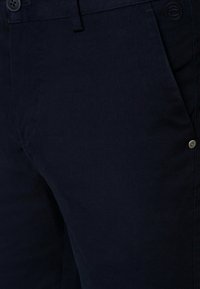 Granatowe spodnie z teksturowanej tkaniny, z zapięciem na guzik, skośną kieszenią i subtelnym detalem z logo na pasku.