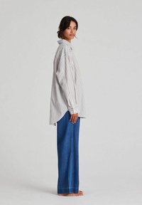 Striped button-up shirt in light gray and white, relaxed fit with a curved hem, paired with wide-leg blue denim jeans, no shoes.