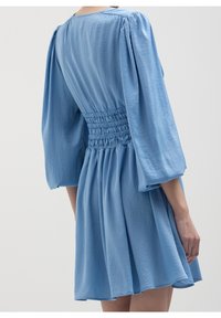 Robe bleue avec de longues manches bouffantes et une taille froncée. Tissu doux, jupe fluide et encolure ronde. Design minimaliste, sans motifs.