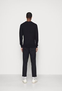 Pull noir à manches longues, col rond et poignets côtelés. Assorti avec un pantalon noir et des baskets blanches. Design simple.