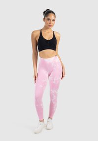Reggiseno sportivo nero e leggings rosa tie-dye. I leggings hanno una texture liscia e vita alta. Il modello indossa scarpe da ginnastica bianche.