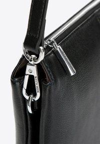Czarna skórzana torebka z metalowymi srebrnymi elementami, z fakturą i zamkiem błyskawicznym. Zawiera klips zaciskowy i detale z logo.