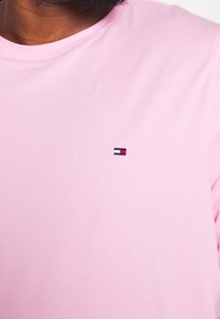 Camiseta de algodón rosa con un pequeño logo bordado en colores rojo, blanco y azul en la parte izquierda del pecho. Mangas cortas, diseño de cuello redondo.