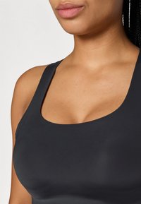 Μαύρο αθλητικό σουτιέν με στρογγυλή λαιμόκοψη και φαρδιές τιράντες, φτιαγμένο από απαλό, ελαστικό ύφασμα. Η υφή φαίνεται ματ και προσαρμόζεται στο σώμα.