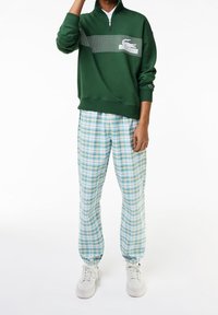 Sweat-shirt vert à fermeture éclair avec un motif en grille sur la poitrine. Assorti à un pantalon à carreaux bleu clair. Des baskets blanches complètent la tenue.