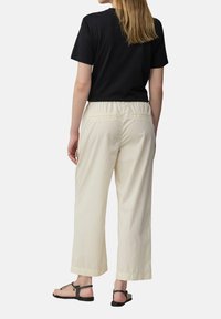 Zwarte korte mouwen t-shirt, crèmekleurige wijde broek met elastische tailleband en zakken, gecombineerd met zwarte sandalen. Neutrale kleurenpalet.