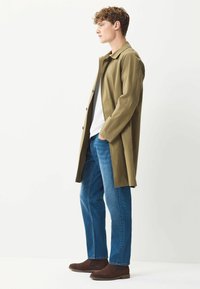 Khaki trencz z kołnierzykiem, niebieskie dżinsy i brązowe zamszowe botki. Slim fit z guzikami i gładką teksturą.