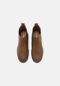 Botas Chelsea de cuero marrón con paneles laterales de elasticidad y lengüetas, con una textura suave y punta redonda. Suela de goma negra.