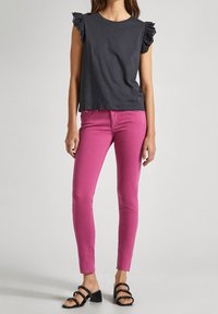 Svart bomullsskjorta med spetsfållärmar, i kombination med slim-fit rosa byxor och svarta sandaler med remmar.