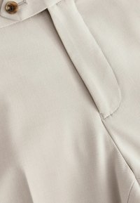 Blusa beige hecha de tela suave, con cierre de botones en la parte delantera, cuello afilado y un corte entallado con detalles de costura sutiles.