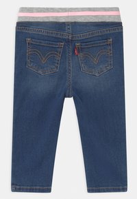 Blå denimjeans med ett grått elastiskt midjeband som har rosa ränder. Två bakfickor med gula sömmar och ett märke vid sömmen.