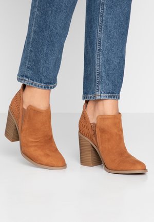 Bottes chevilles en daim marron avec un motif tissé sur les côtés et un petit talon empilé. Les bottes disposent d'une fermeture éclair latérale pour un enfilage facile.