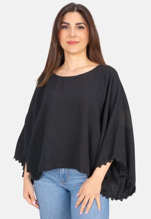 Schwarzes Poncho-Oberteil aus leichtem strukturiertem Stoff, mit weiten Ärmeln und Spitzenbesatz am Saum, kombiniert mit blauen Jeans.