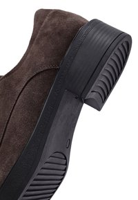 Brown suede shoe with a rounded toe, featuring a black rubber sole with textured ridges and a smooth, curved heel.