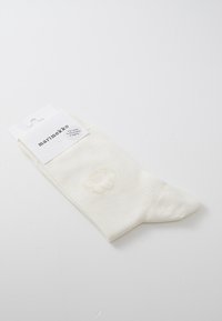 Calzino di cotone bianco con un delicato design a fiore giallo, texture a coste e un'etichetta con il marchio e i dettagli del prodotto in cima.