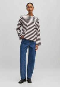 Gestreepte lange mouwen top in bruin en wit, gecombineerd met high-waisted blauwe spijkerbroek. Zwarte leren enkellaarsjes maken de outfit compleet.