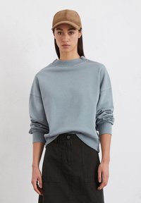 Lichtblauwe sweatshirt met een ronde halslijn en opgerolde mouwen, gecombineerd met een donkergroene rok met voorzakken en een knoopsluiting.