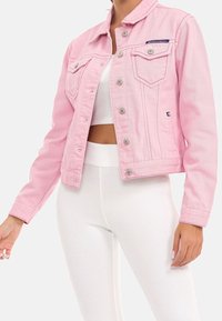 Rosa denimjacka med krage, tryckknappar och två framfickor. Buren över en vit ribbad topp och matchande byxor.