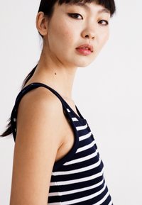 Navy and white striped sleeveless top, ribbed texture, round neckline, button accents, fitted design, smooth material, casual style.