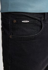 Czarne dżinsy o prostym kroju z przednią kieszenią, nitami i prostokątną metką marki "PETROLIND". Teksturowana tkanina o delikatnym połysku.