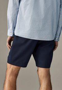 Shorts bleumarin dintr-un material ușor, cu o croială lejeră și un tiv curat. Foarte bine asortați cu o cămașă cu butoni, de culoare albastră deschis, cu dungi.