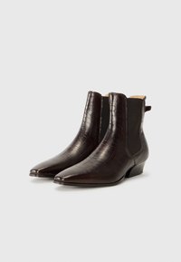 Bottines en cuir synthétique crocodile marron avec des bouts pointus, des panneaux élastiques sur les côtés et un petit talon. Texture lisse avec un léger éclat.
