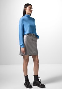 Maglione a collo alto blu, mini gonna metallica argento e stivali da combattimento neri con lacci. Texture liscia, design aderente e colori a contrasto.