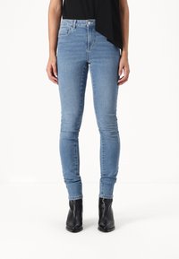 Jeans skinny azuis claros feitos de denim com uma cintura alta, apresentando um bolso frontal e barras dobradas nos tornozelos, combinados com botins pretos.